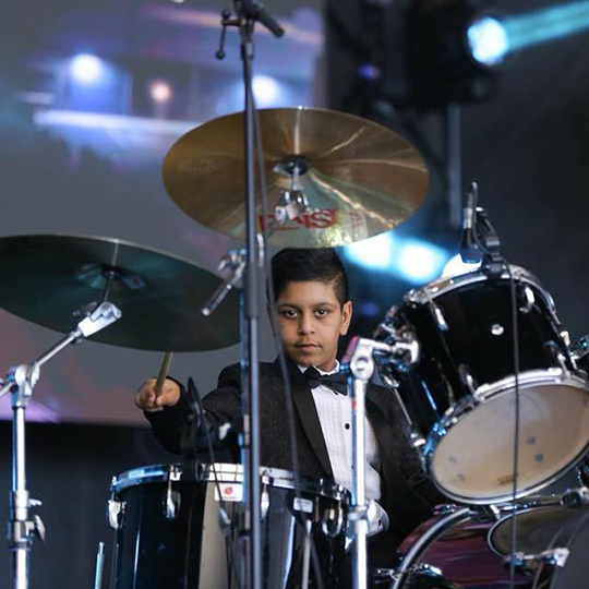Drummer performing on stage, elegant attire.
